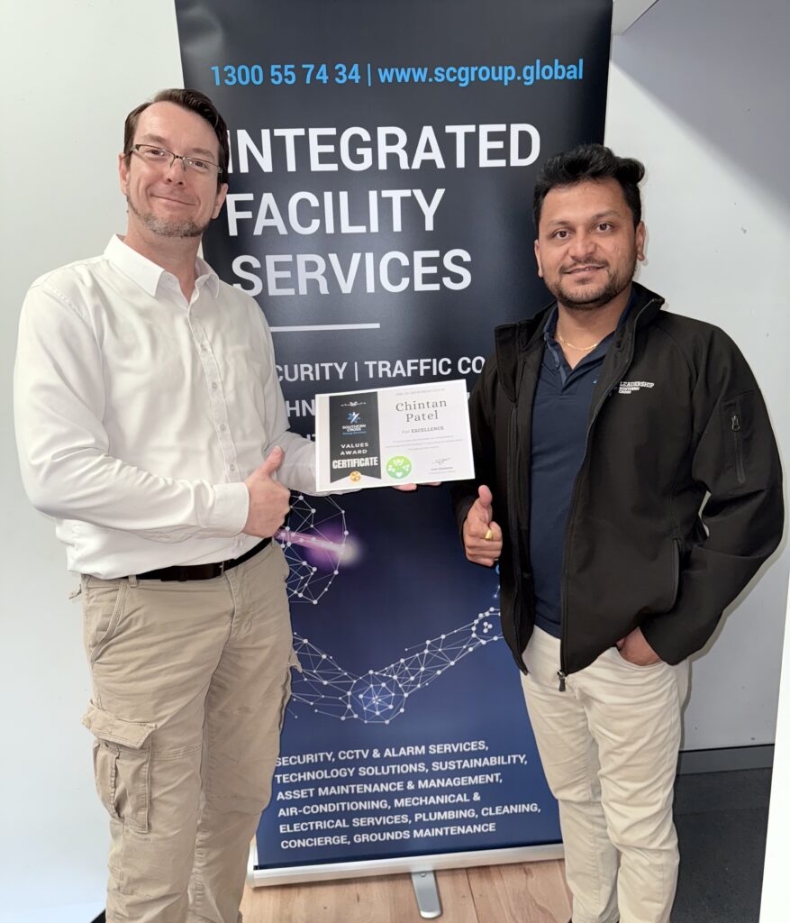 Chintan Patel holds an award certificate for Excellence while standing next to Stuart Moran, MBA, who is presenting the award. Both are smiling in front of Southern Cross Group branding.